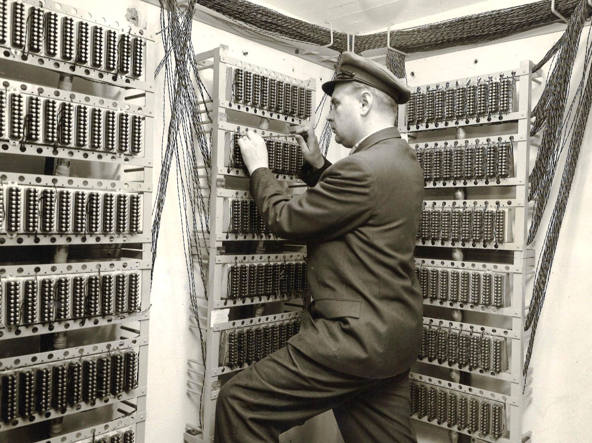A technician on a step reaches into tall racks of telephone relays