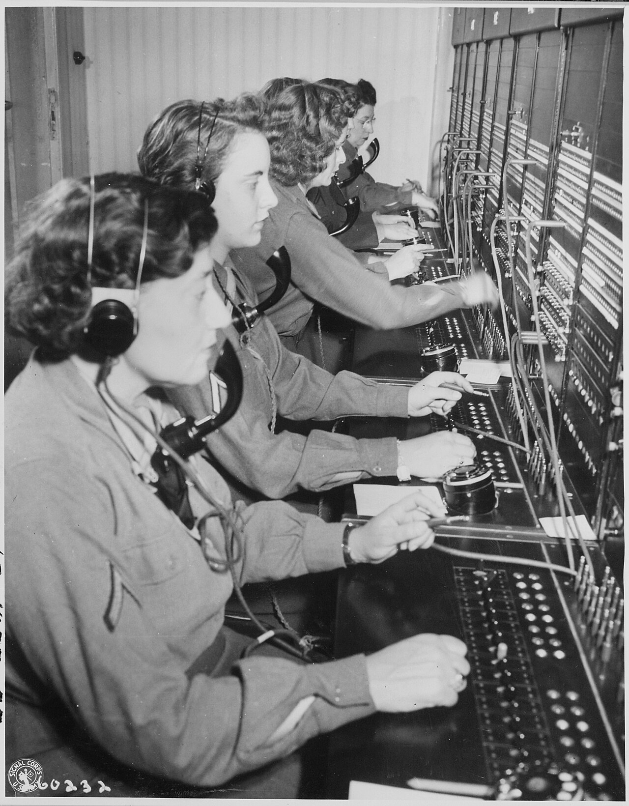 Operators wearing headsets work a row of switchboard positions